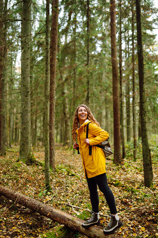 A woman in a yellow raincoat walks in the woods in Vermont, where our Barre addiction treatment center is located.