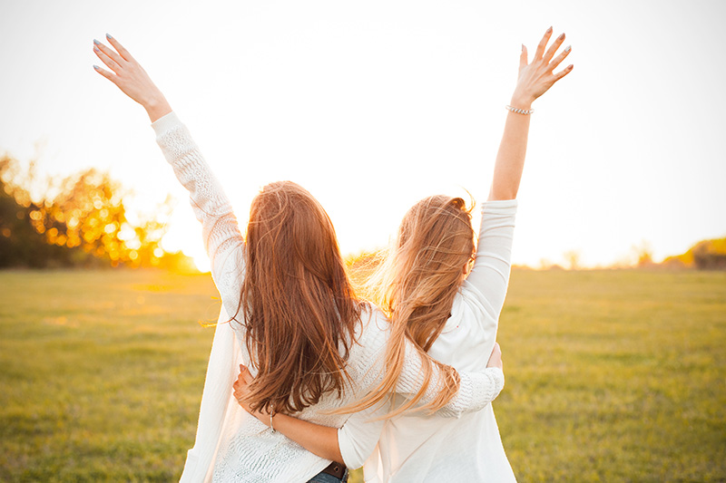 Two friends face away from the camera and hold up their arms in joy.