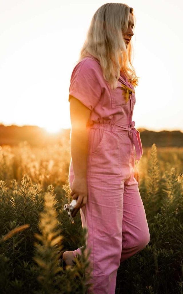 a woman in a pink jumpsuit standing in a field